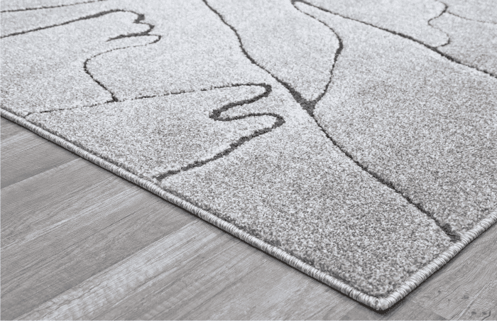Alto texto: Alfombra beige con líneas curvas y detalles geométricos, ideal para decorar espacios modernos y acogedores en el hogar u oficina.