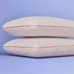 Alto en texto alternativo: Dos cojines decorativos en tono beige con acabado texturizado sobre fondo azul claro.