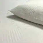 Cojín y ropa de cama en tonos beige con patrones geométricos y texturas suaves para decorar dormitorios y crear ambientes acogedores.