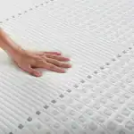 Borrador de imagen de un colchón de color blanco con textura de patrones geométricos y una mano tocándolo para mostrar su superficie suave y cómoda.