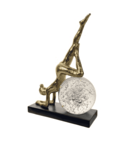 Escritorio con decoración de figura de una persona haciendo yoga y una esfera decorativa, en colores dorados y plateados, ideal para complementar un ambiente de sala o despacho.