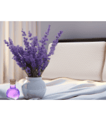 Lavanda en jarrón blanco sobre cama con almohada ortopédica, cerca de una pequeña botella de perfume. Decoración elegante y relajante para dormitorios, con muebles y sillones de estilo moderno.